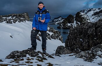 Der Ökologe Fritz Hertel steht in dicker Winterbegleitung auf einem kleinen Felsen in der Antarktis