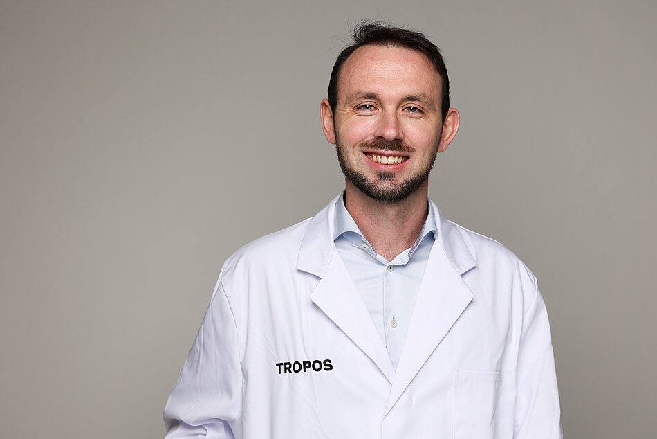 Dr. Sebastian Zeppenfeld trägt einen weißen Kittel und lächelt in die Kamera.
