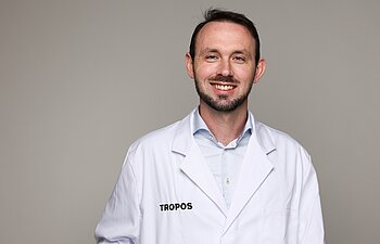 Dr. Sebastian Zeppenfeld trägt einen weißen Kittel und lächelt in die Kamera.
