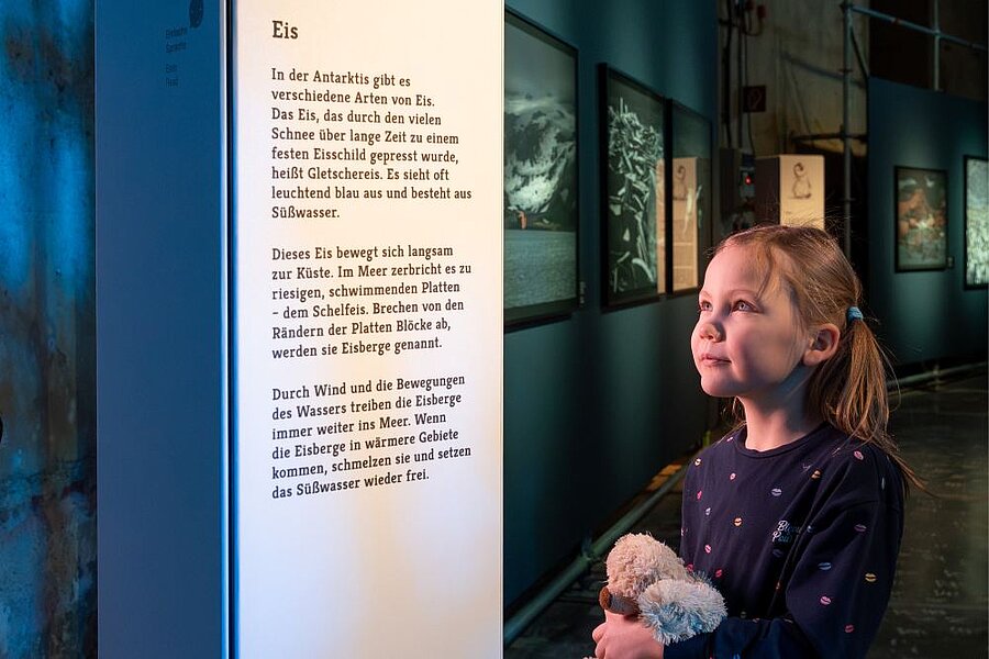 junges Mädchen mit Kuscheltier in der Hand betrachtet eine Stele in der Ausstellung ANTARKTIS
